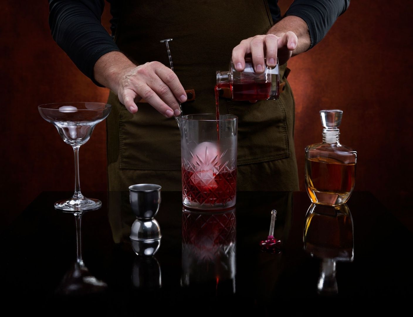Bartender schenkt een rode cocktail in een geslepen mengglas