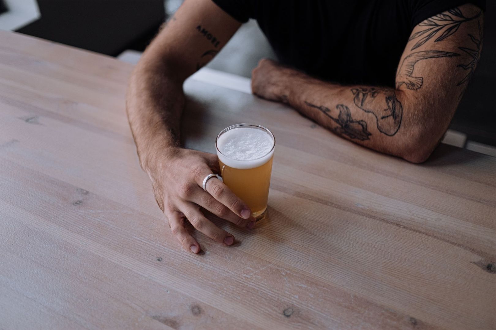 Hand met ring naast een glas goudkleurig bier met schuim op houten tafel